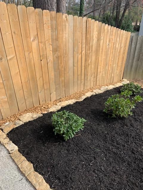 A wooden fence surrounds a bed of mulch and plants.