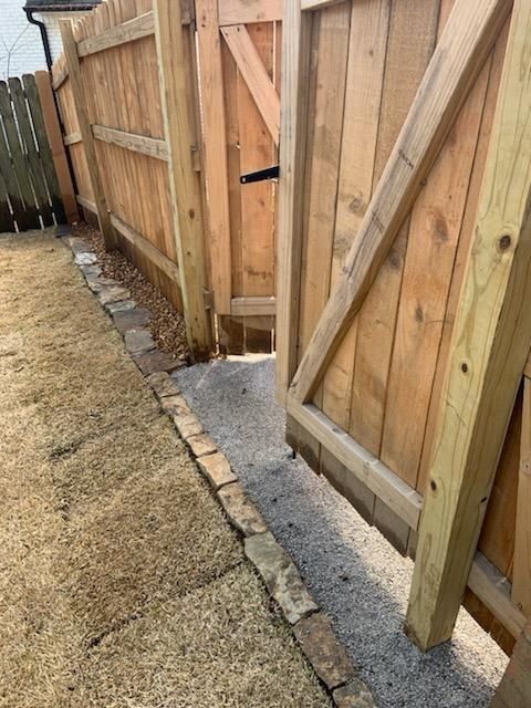 Wooden fence with a gate, gravel path, and bordering bricks.