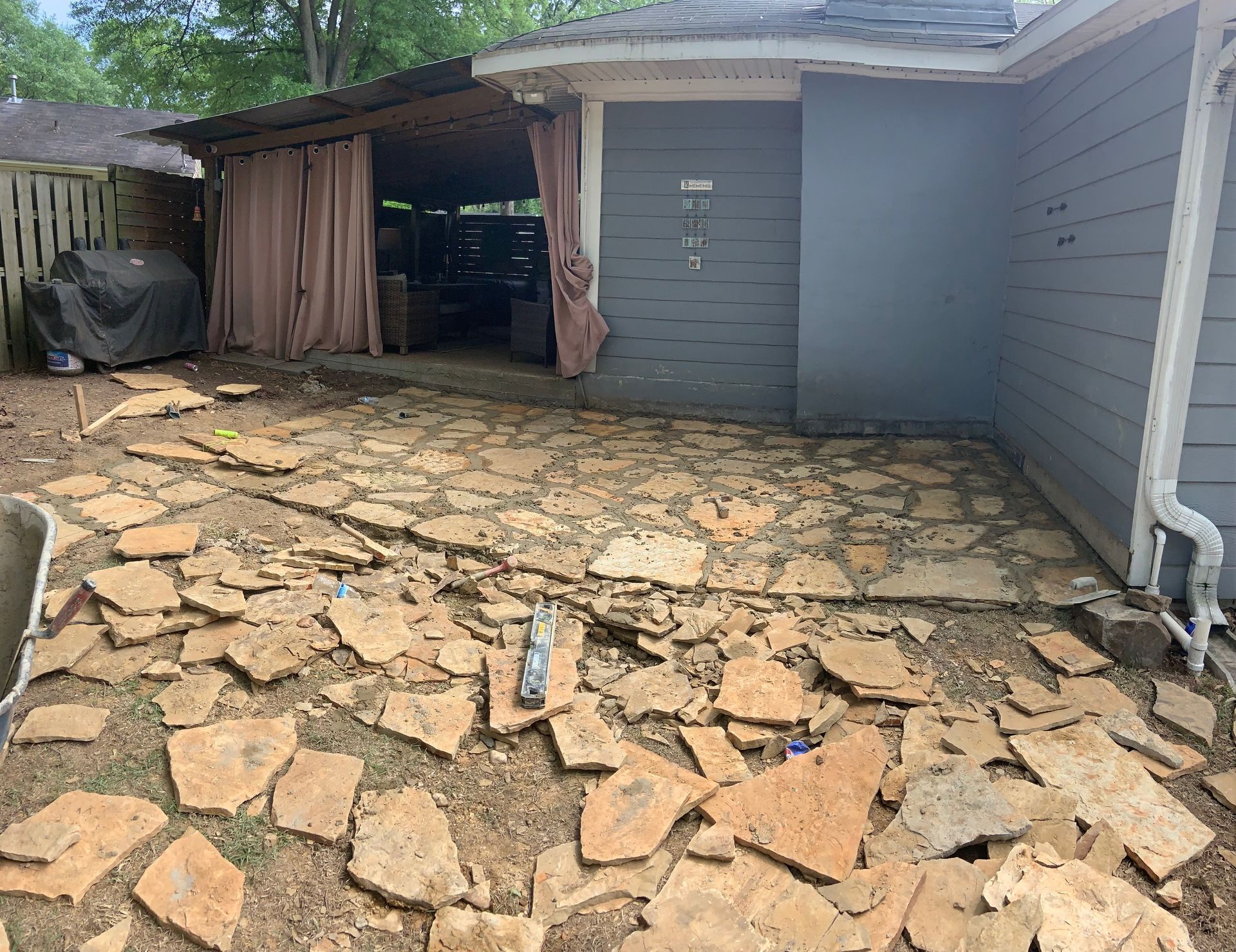 Outdoor patio with torn-up stone paving. A covered area with curtains is visible.