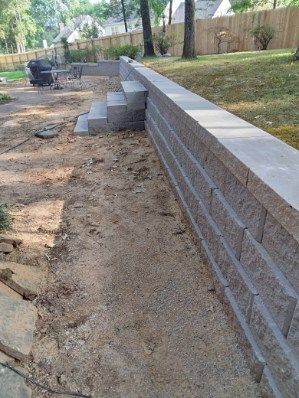 Stone retaining wall with steps, in a yard with a grassy hill in the background.