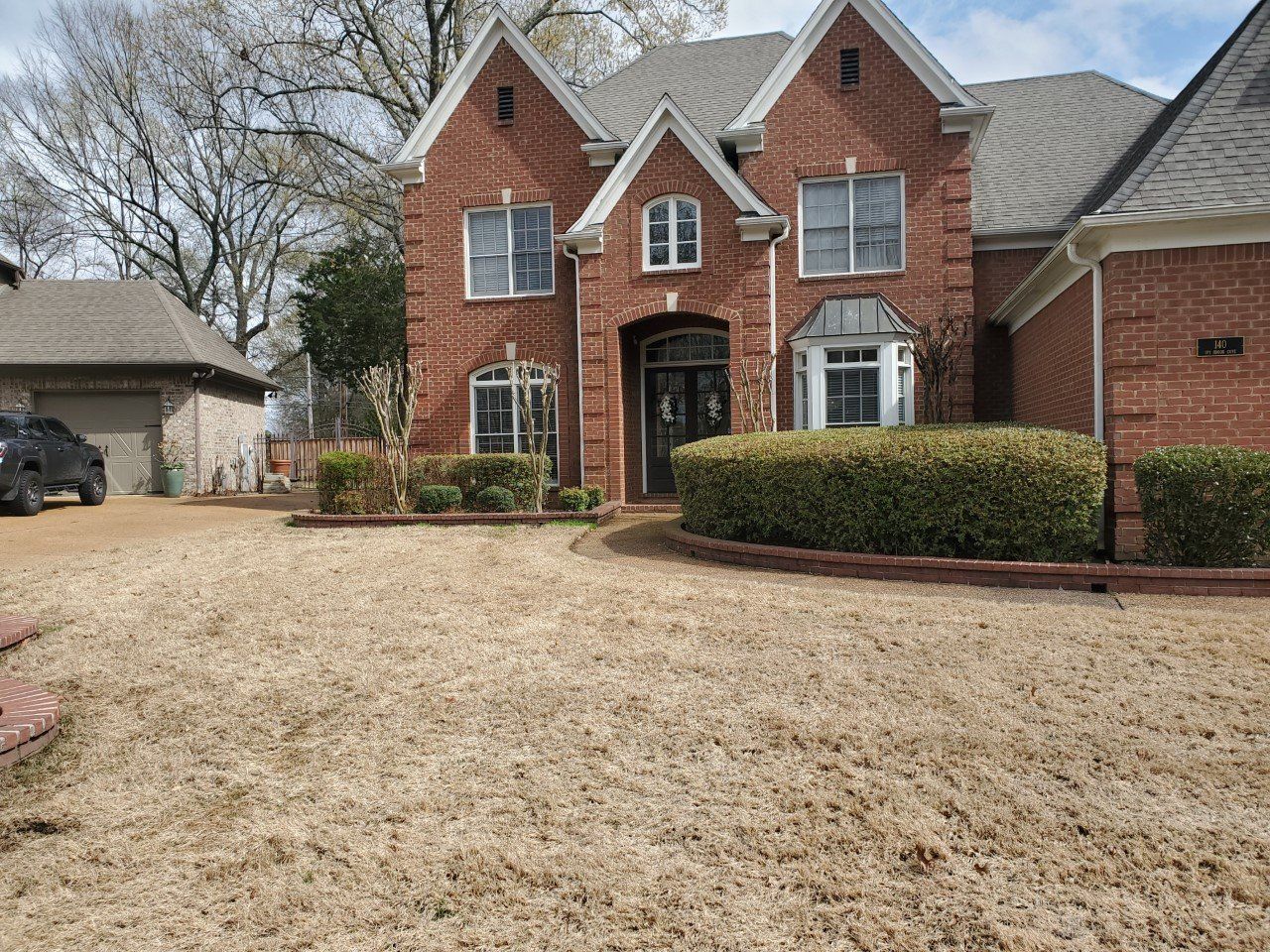 Brick house with a dry brown lawn and a detached garage.