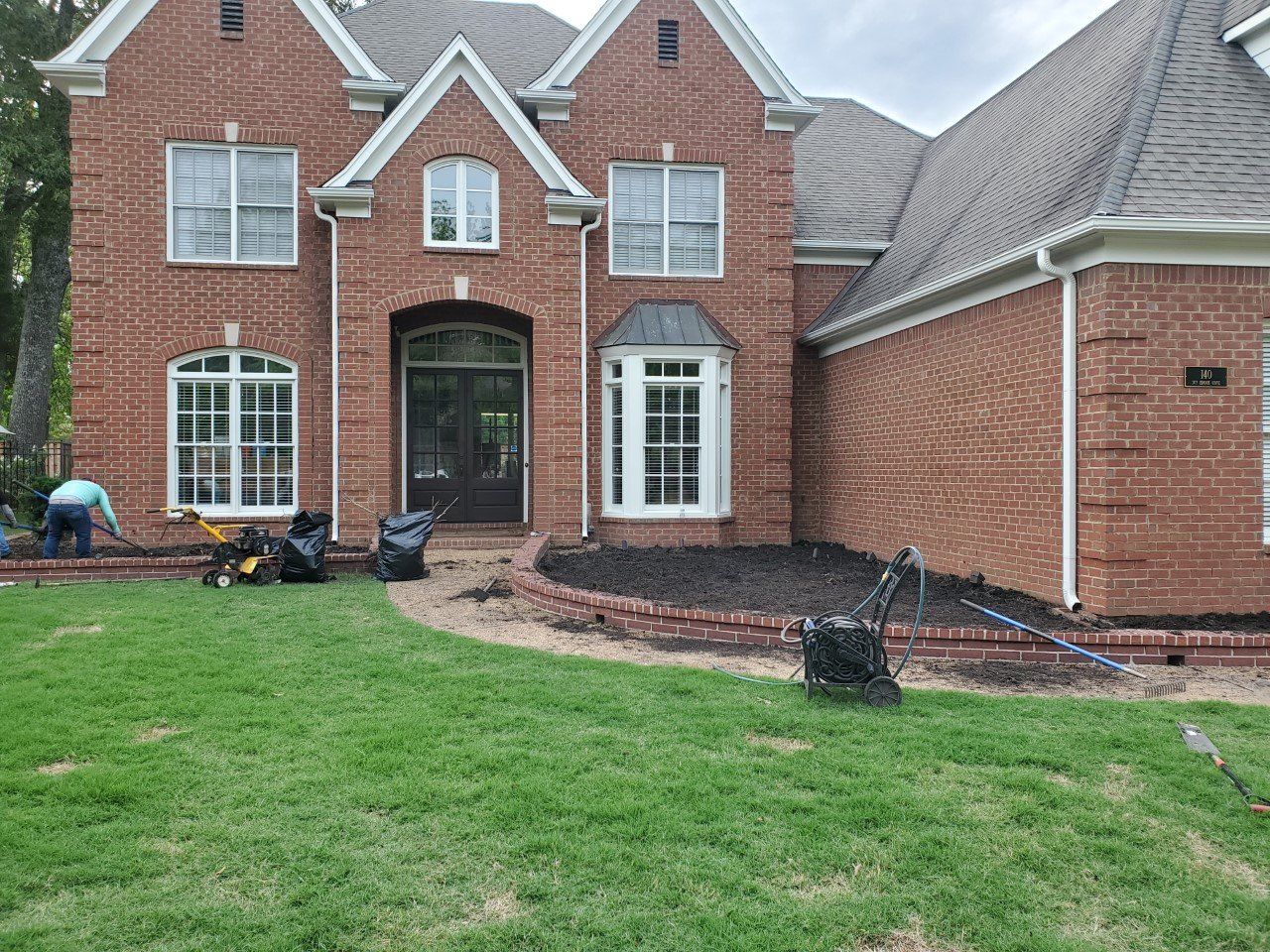 Brick home with landscaping being worked on; green lawn in foreground.
