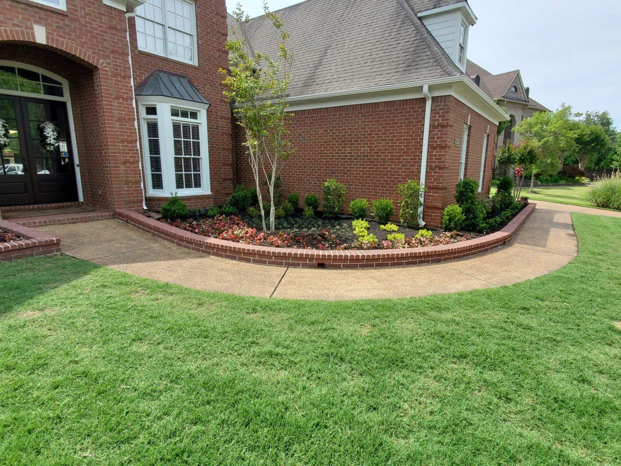 Brick home with a curved walkway and landscaped flower beds. Green grass surrounds.
