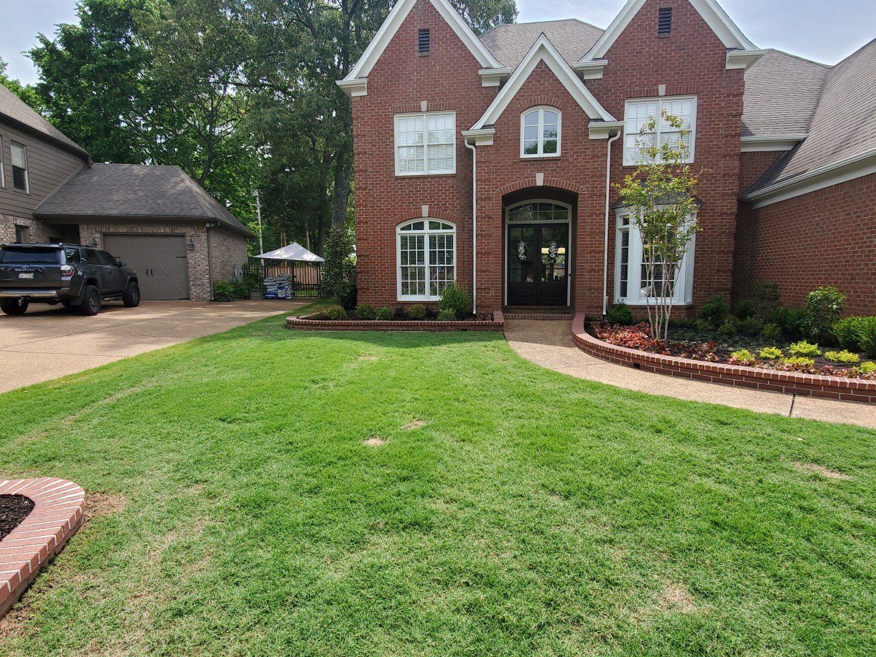 Two-story brick house with green lawn, driveway, and a small garage.