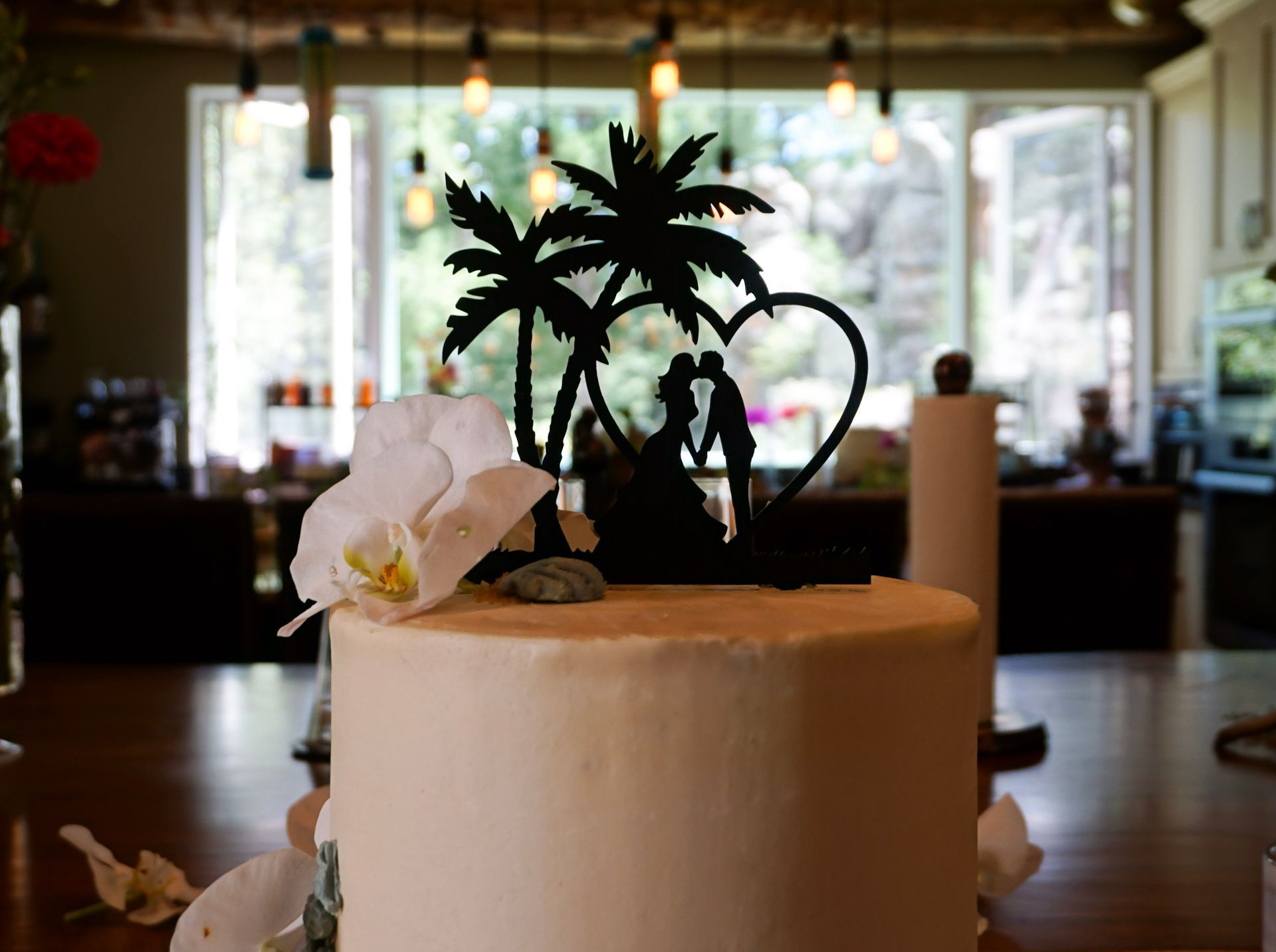 White cake with orchid and palm tree topper in a softly lit restaurant setting
