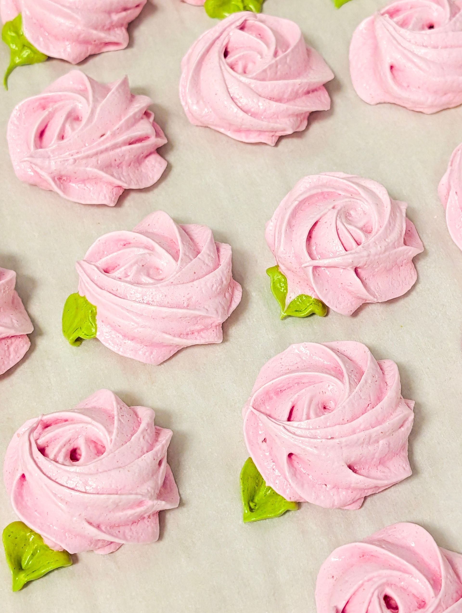 Pink rose-shaped meringues with green leaves on a light background