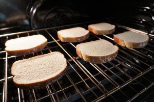 Slices of bread toasting on an oven rack under a broiler
