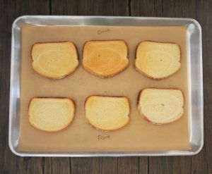 Tray with six toasted bread slices arranged in two rows on parchment paper