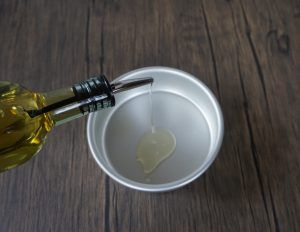 Olive oil being poured from a bottle into a small white bowl on a wooden surface.