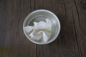White tissue paper in a small metal bowl on a dark wooden surface.