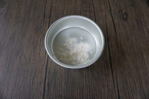 A metal bowl of water with a small white mound, resting on a dark wooden table.