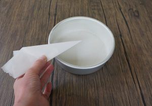 Hand holding a paper towel above a white bowl of water on a wooden table