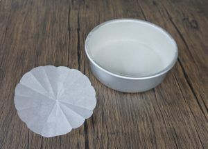 White bowl and round coffee filter on a wooden surface.