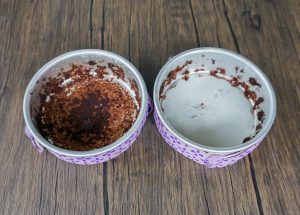 Two small white bowls on a wooden table, one with dark residue and one mostly empty with crumbs.