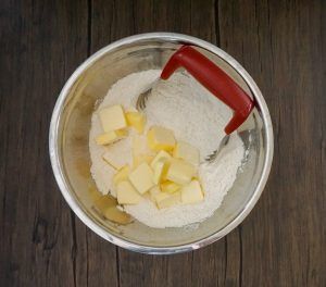 Mixing bowl with flour, butter cubes, and a red spatula on a wooden surface