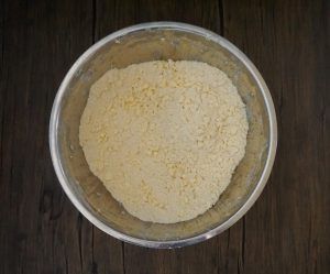 A metal bowl filled with pale yellow flour on a dark wooden surface