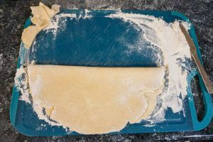 Blue tray with spilled flour and dough on a countertop, with a rolling pin at the right edge