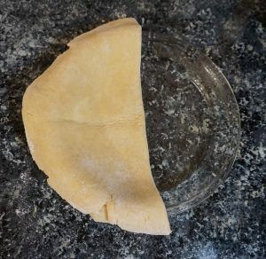 A broken beige tortilla chip on a dark speckled countertop next to a clear glass rim.