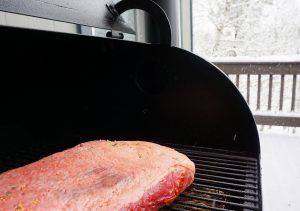 Raw steak on a grill outdoors, with a black grill hood and patio railing in the background