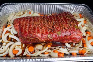 Seasoned raw rib roast in a foil pan with sliced onions and carrots, ready for cooking