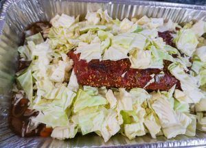 Foil tray with shredded lettuce topped by a glazed rib or meat strip
