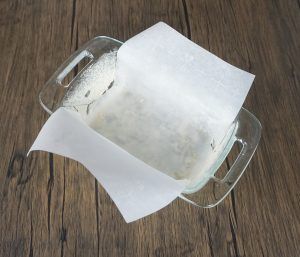Glass baking dish lined with parchment paper on a wooden table