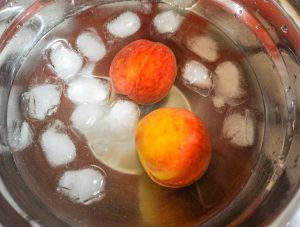 Two oranges floating in a bowl of water with ice cubes