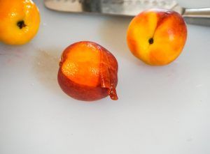 Three small orange-red fruits on a white surface, one with a brown blemish.