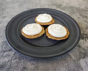 Three frosted cookies on a black plate on a gray countertop