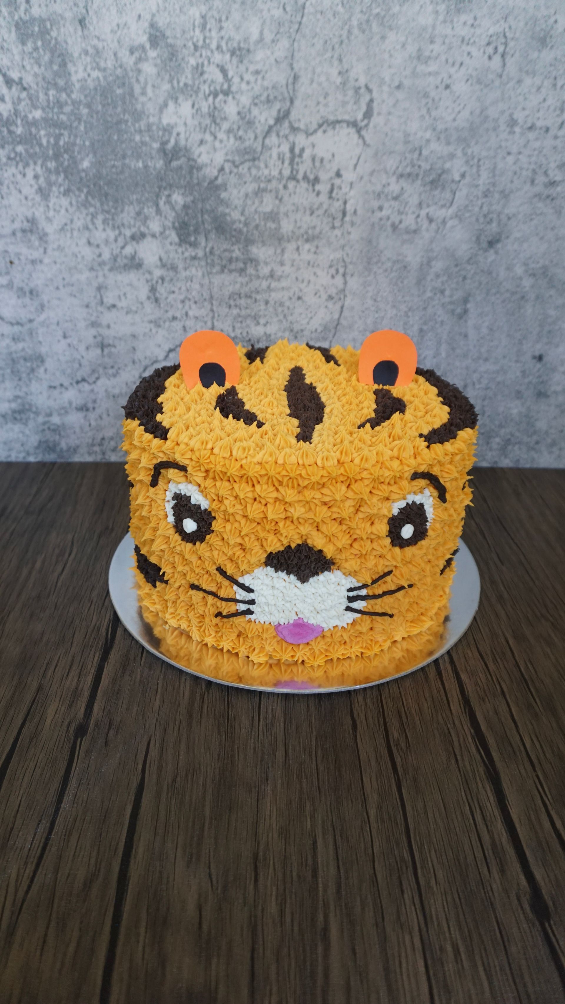 Orange tiger cake with black stripes and white muzzle on a wooden table against a gray wall