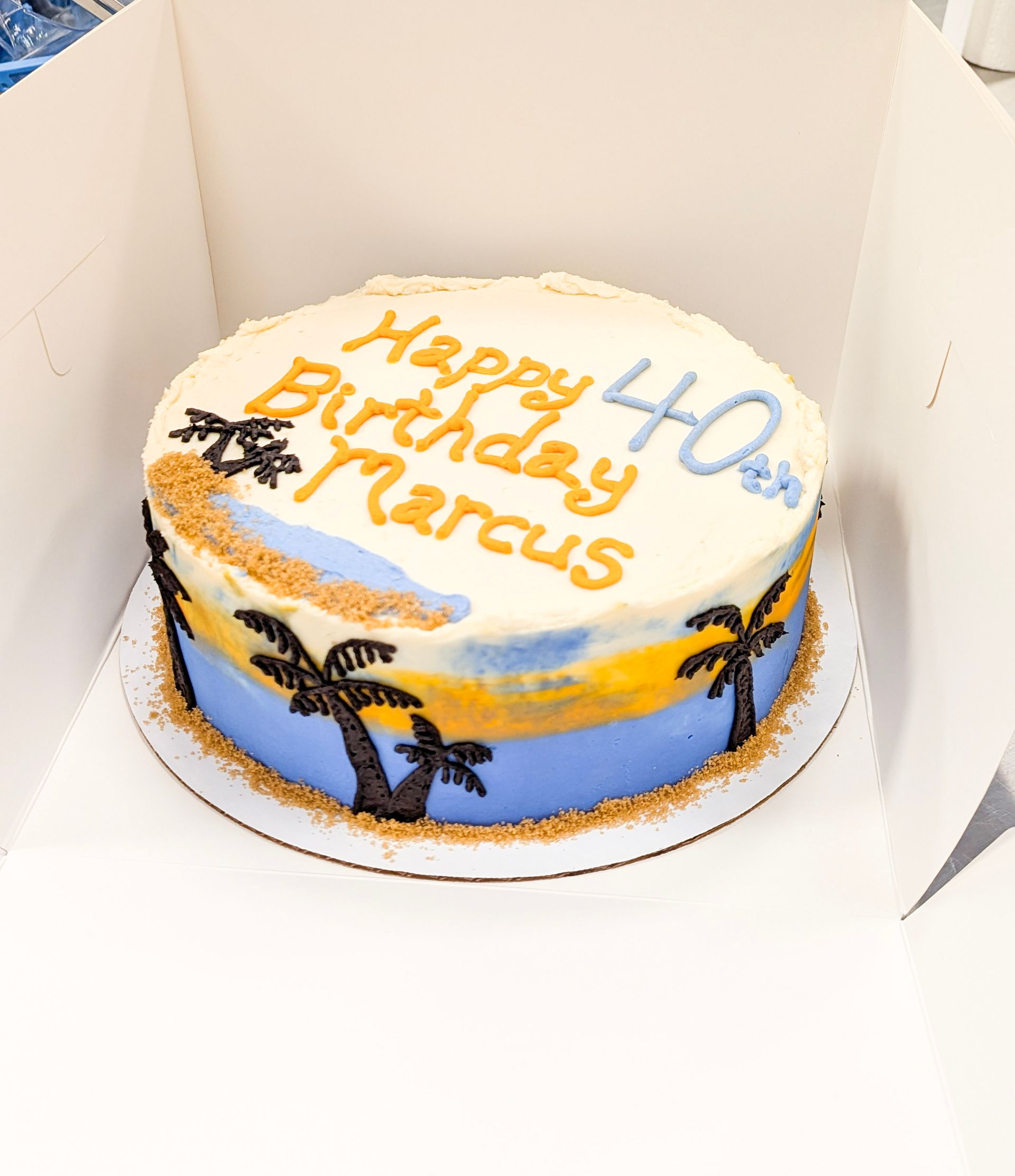 Happy 40th birthday Marcus cake with palm trees and blue-yellow icing in a white box