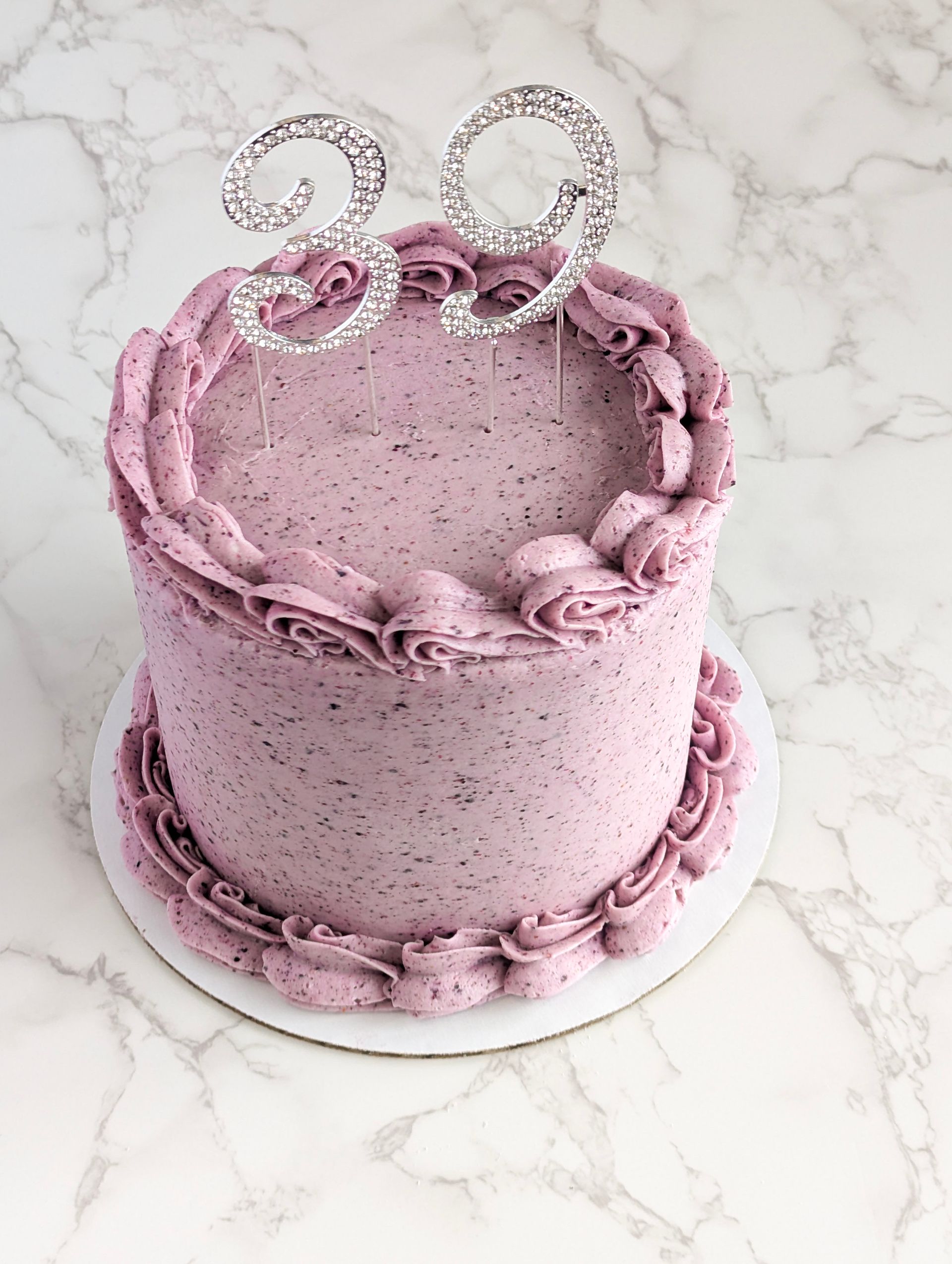 Pink frosted cake with pearl trim and a sparkling “29” topper on a white marble surface