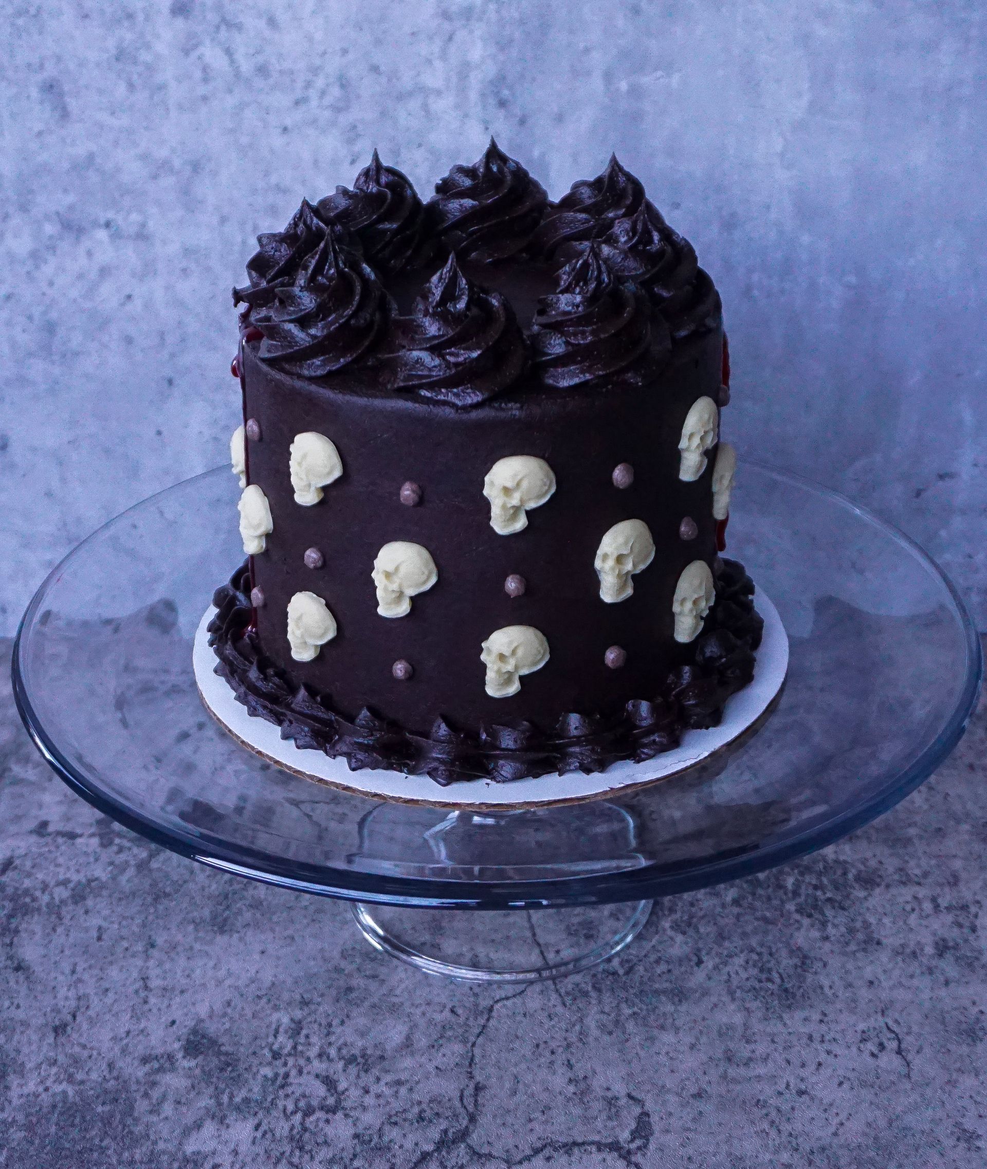 Chocolate cake with dark frosting and white skull decorations on a glass cake stand