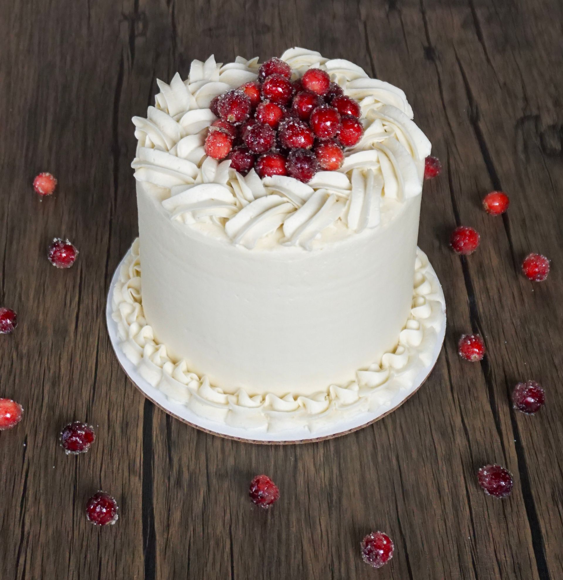 White frosted cake topped with red berries on a rustic wooden table