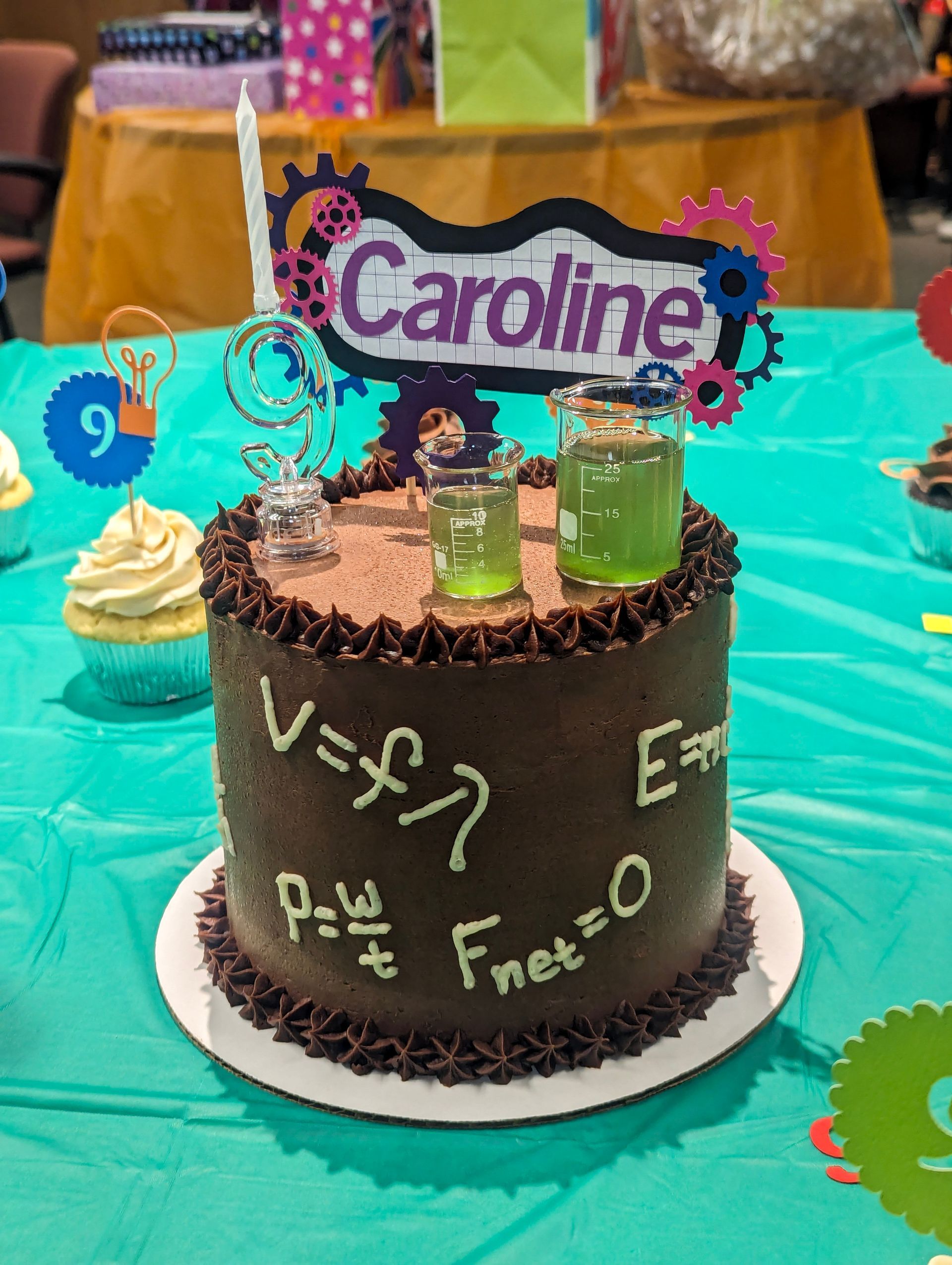 Chocolate birthday cake with a “Caroline” topper, lab-themed decorations, and a turquoise party table