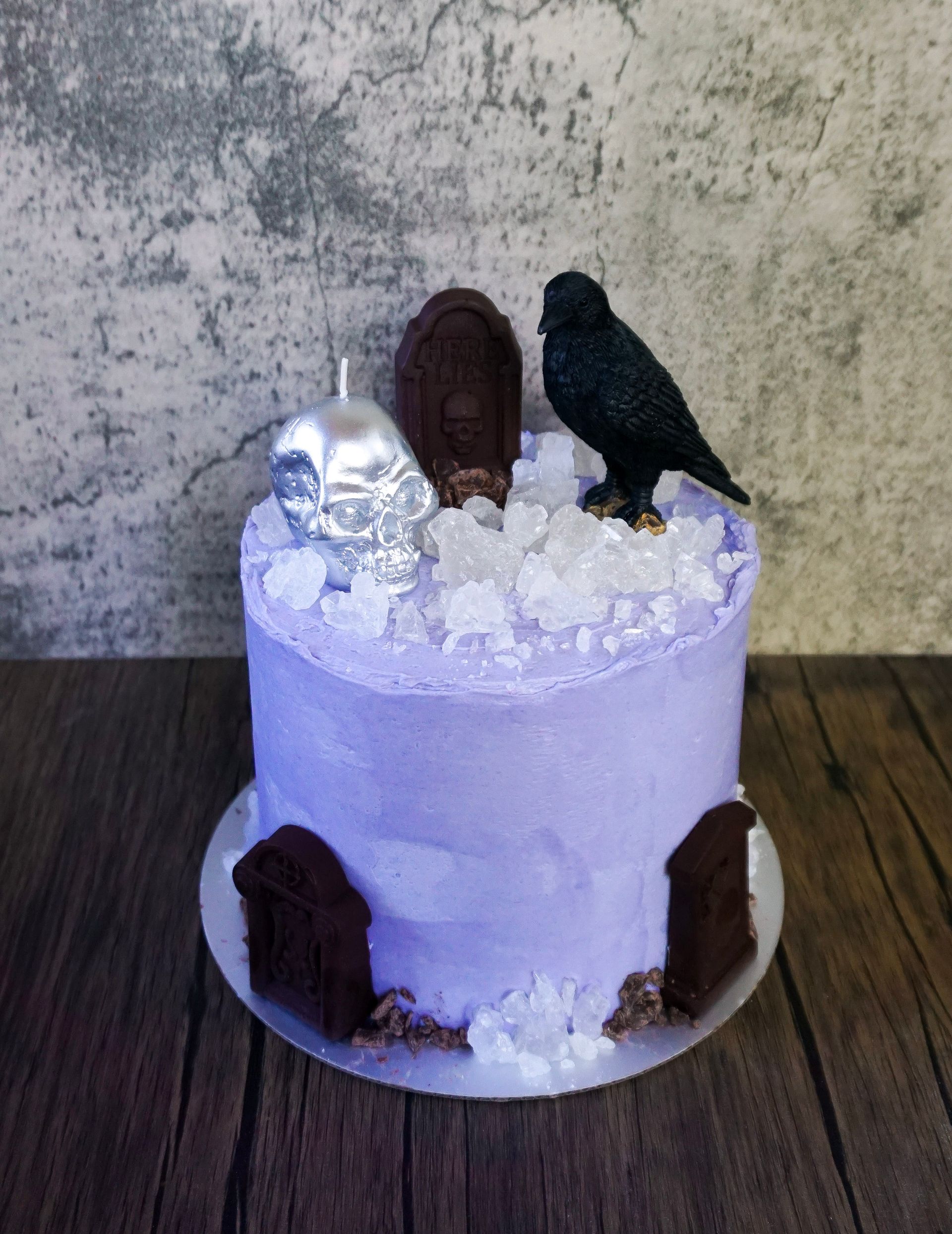 Purple frosted cake decorated with black bird figurine, silver ornament, and brown door accents