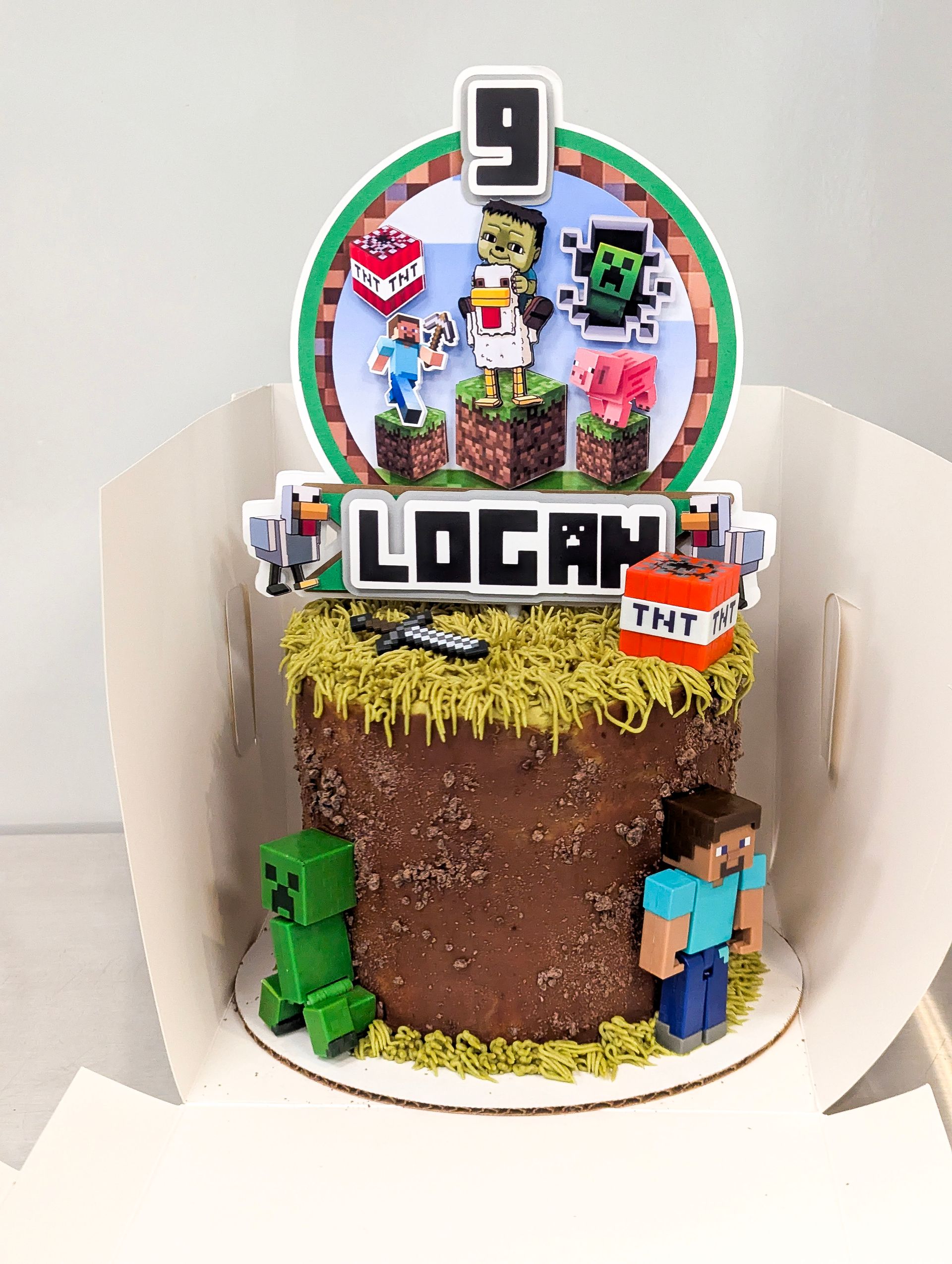 Minecraft-themed birthday cake with “9” topper and “LOGAN” name plaque, decorated with game characters and blocks