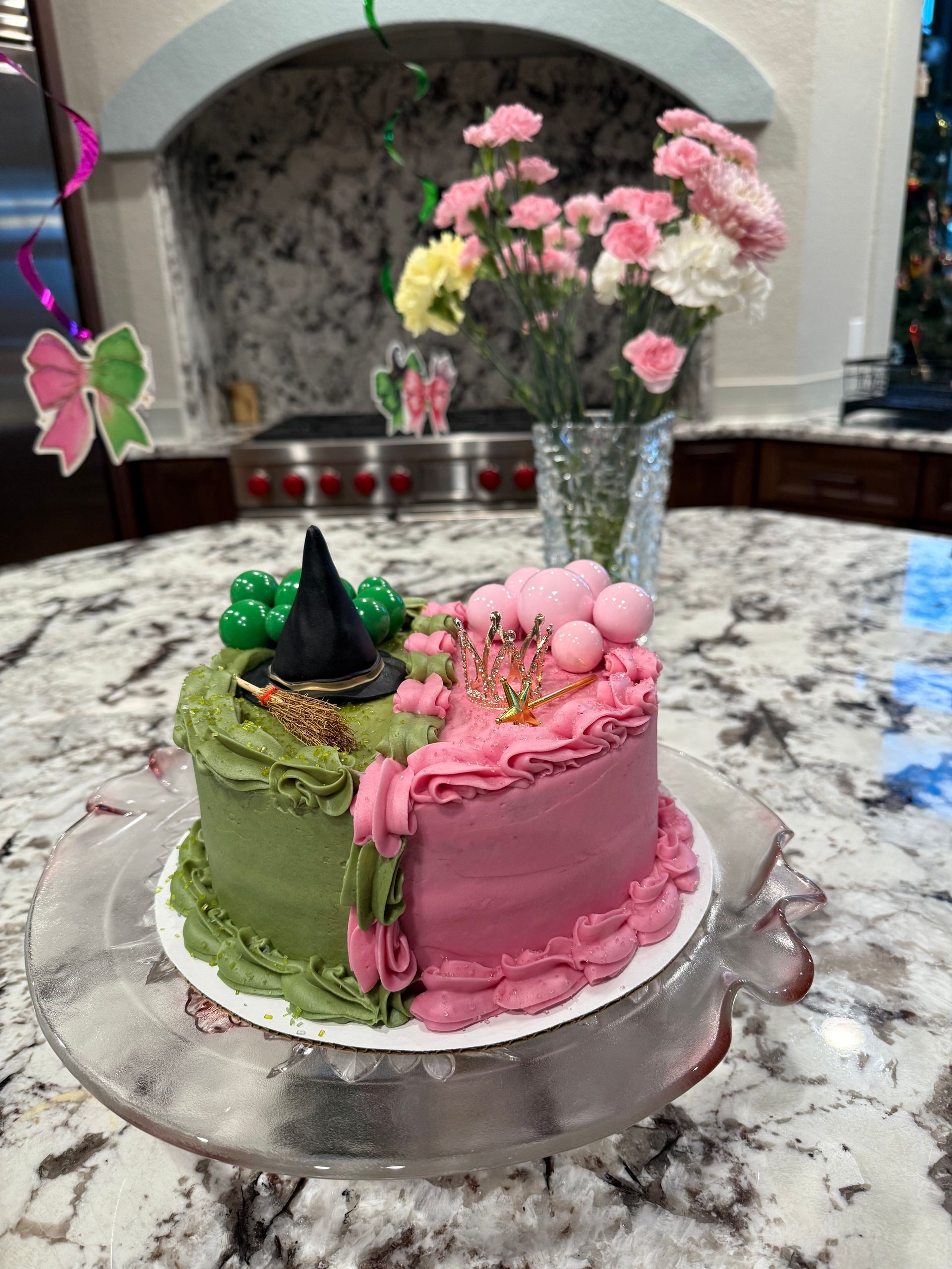 Half pink, half green decorated cake with flowers and a party hat on a marble counter