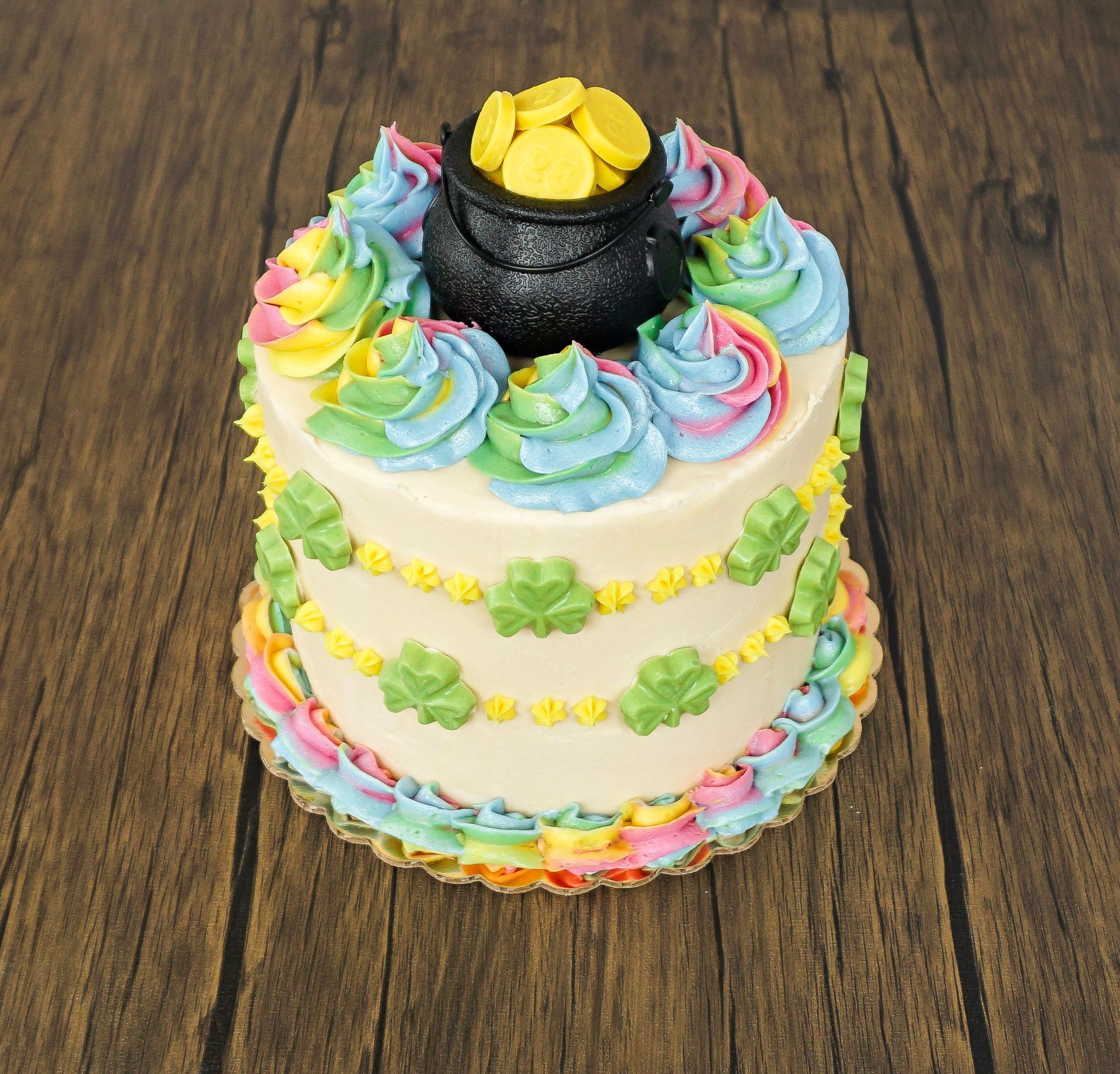Decorated pastel layer cake with rainbow frosting flowers and a black-and-yellow top decoration on a wooden table