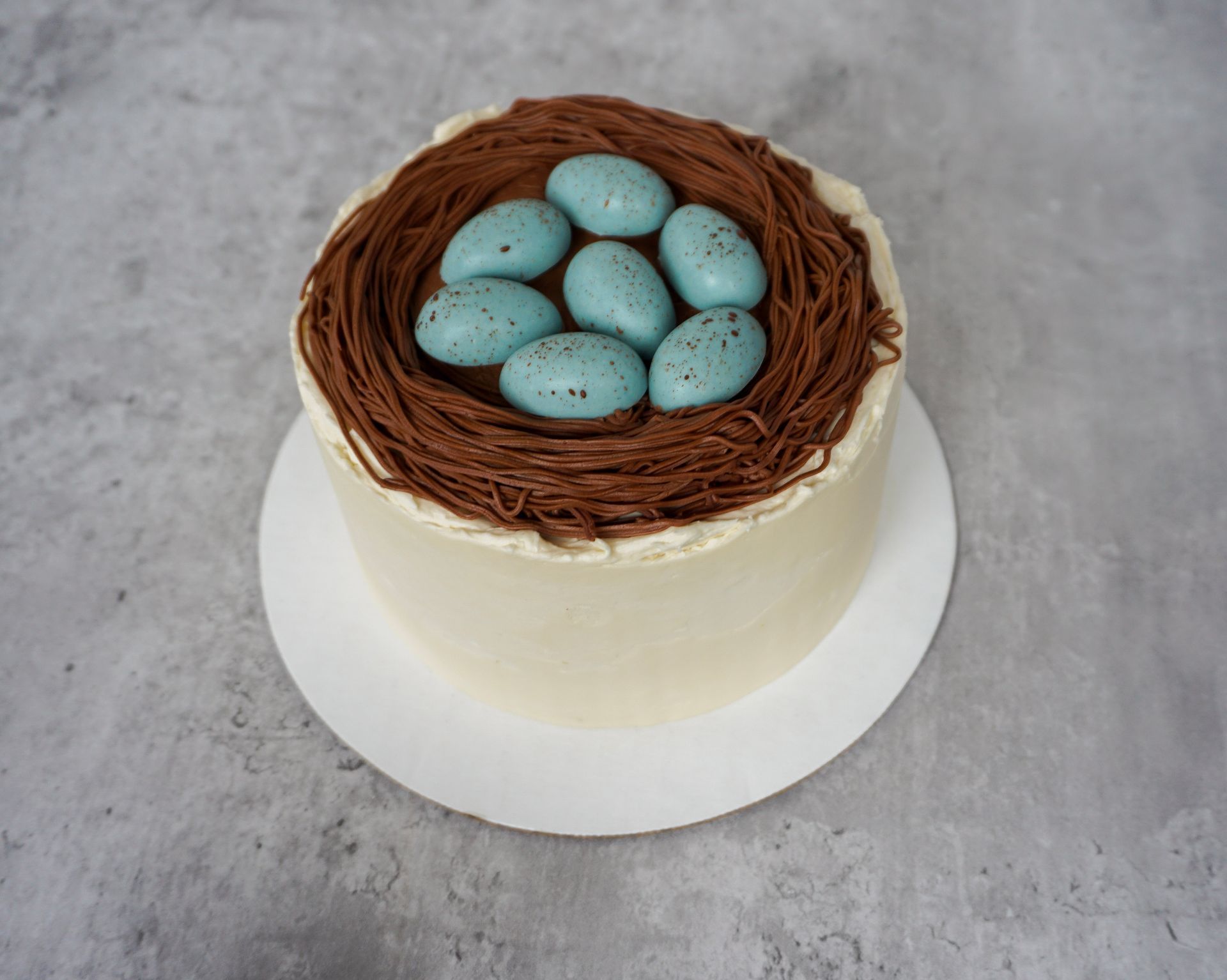Cake topped with a chocolate nest and blue speckled eggs on a white cake board