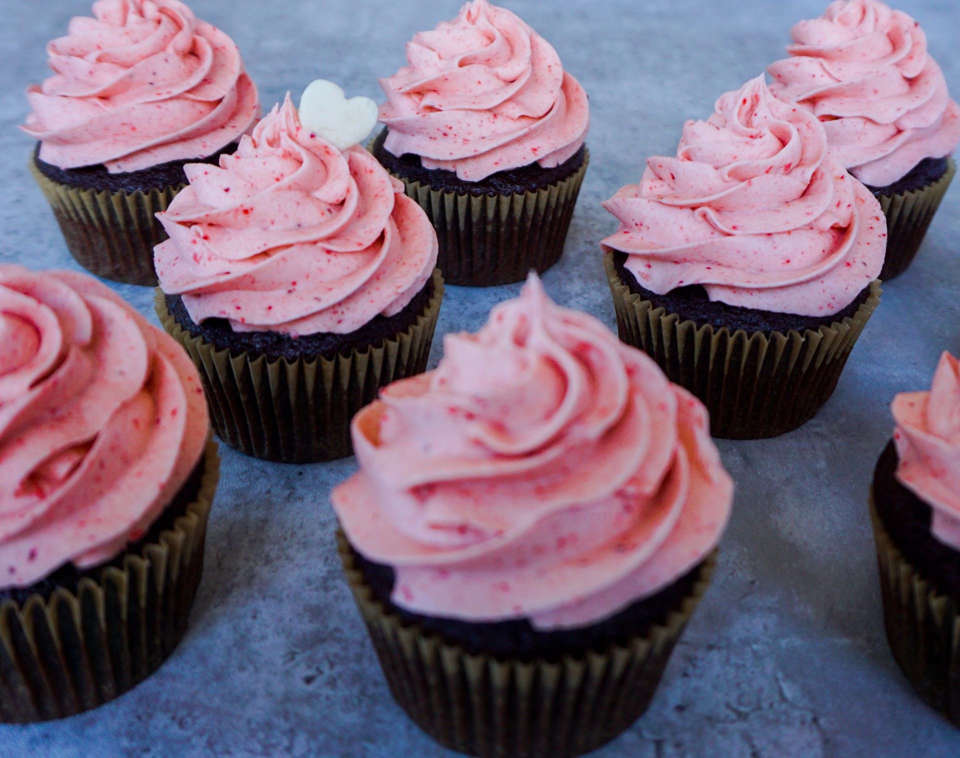 Chocolate cupcakes with pink frosting arranged on a blue surface