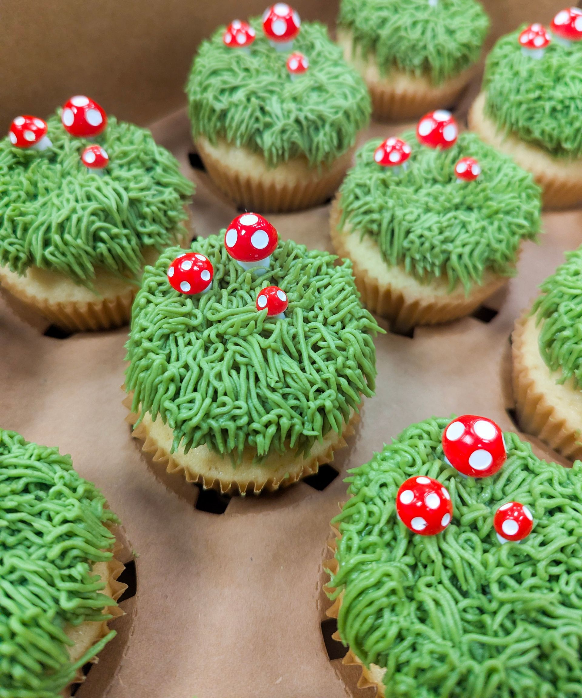 Green frosted cupcakes topped with red-and-white mushroom decorations on a baking tray