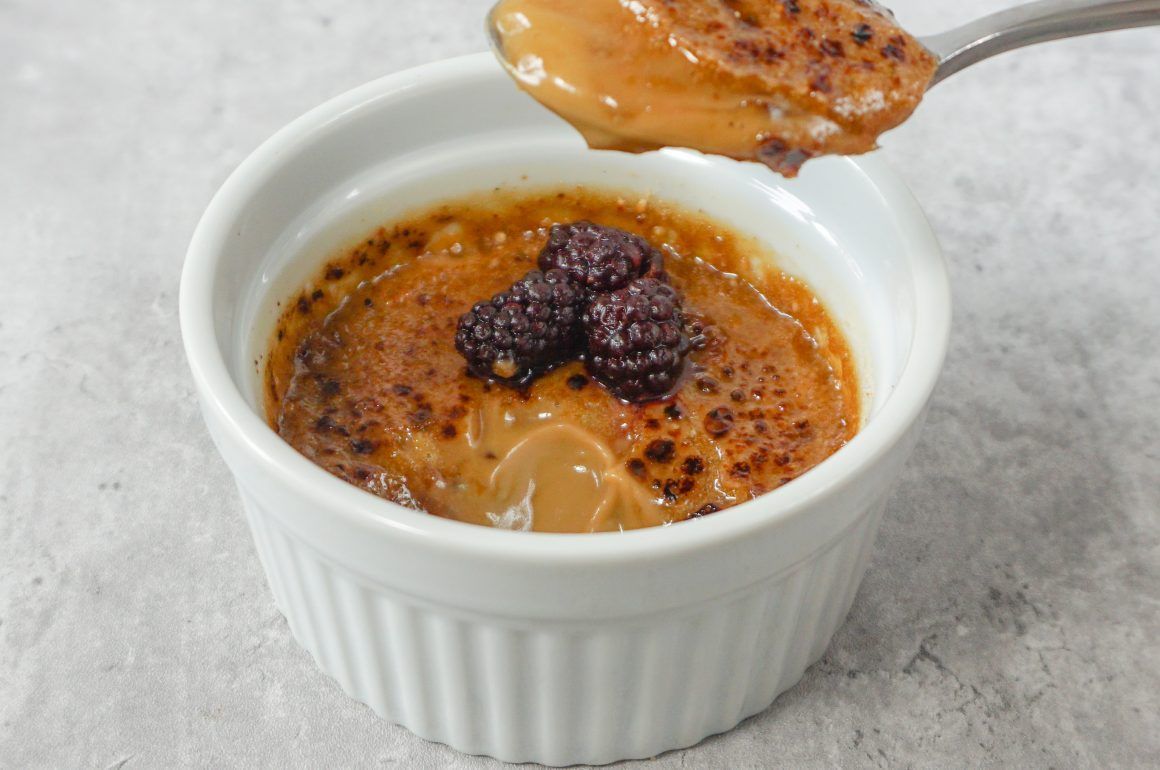 Crème brûlée in a white ramekin with caramelized sugar and a spoonful lifted above it