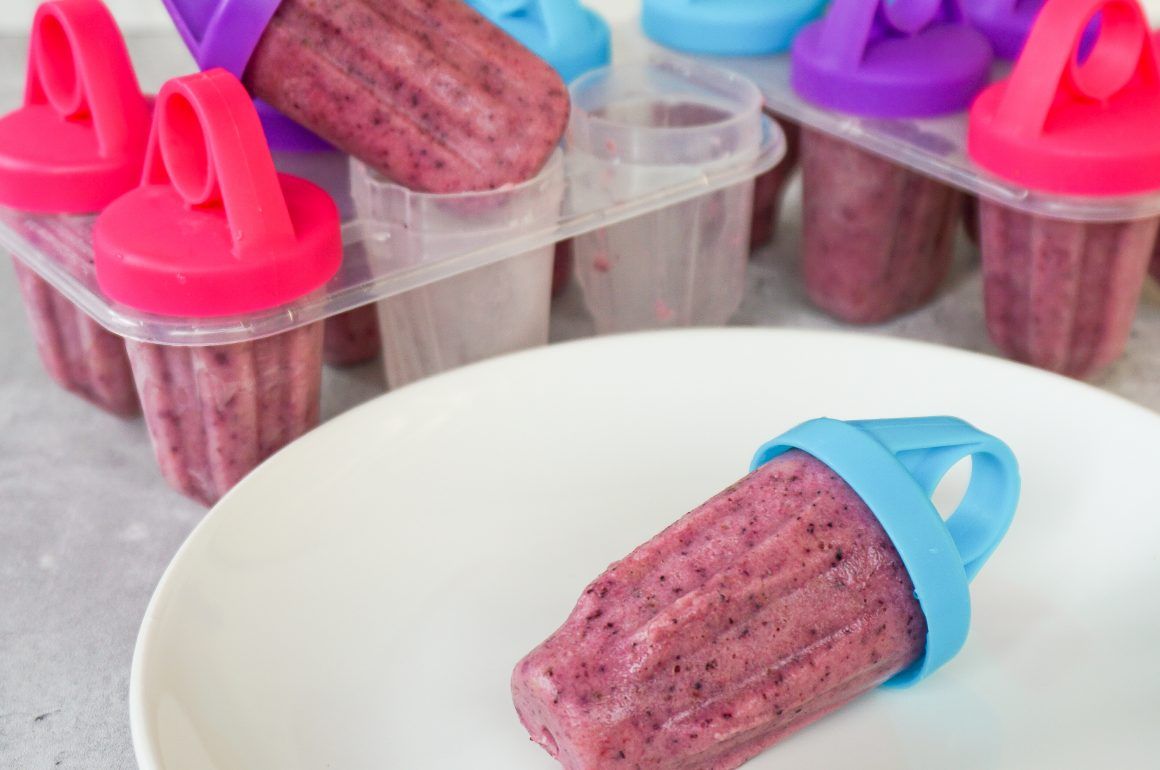 Pink berry popsicles in clear molds with colorful handles on a white surface