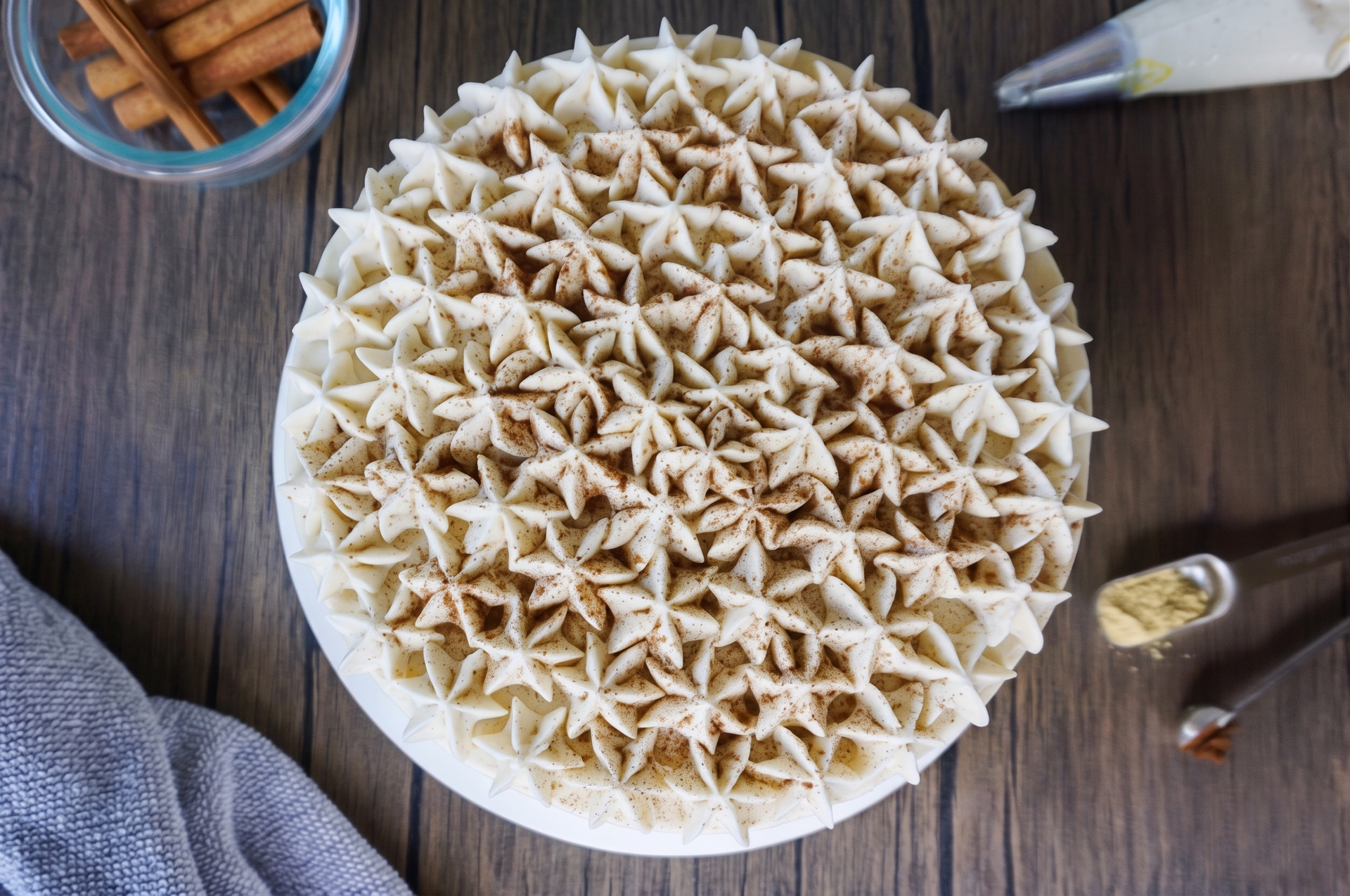 Top-down view of star-shaped cookies arranged on a white plate on a wooden table with a piping bag nearby