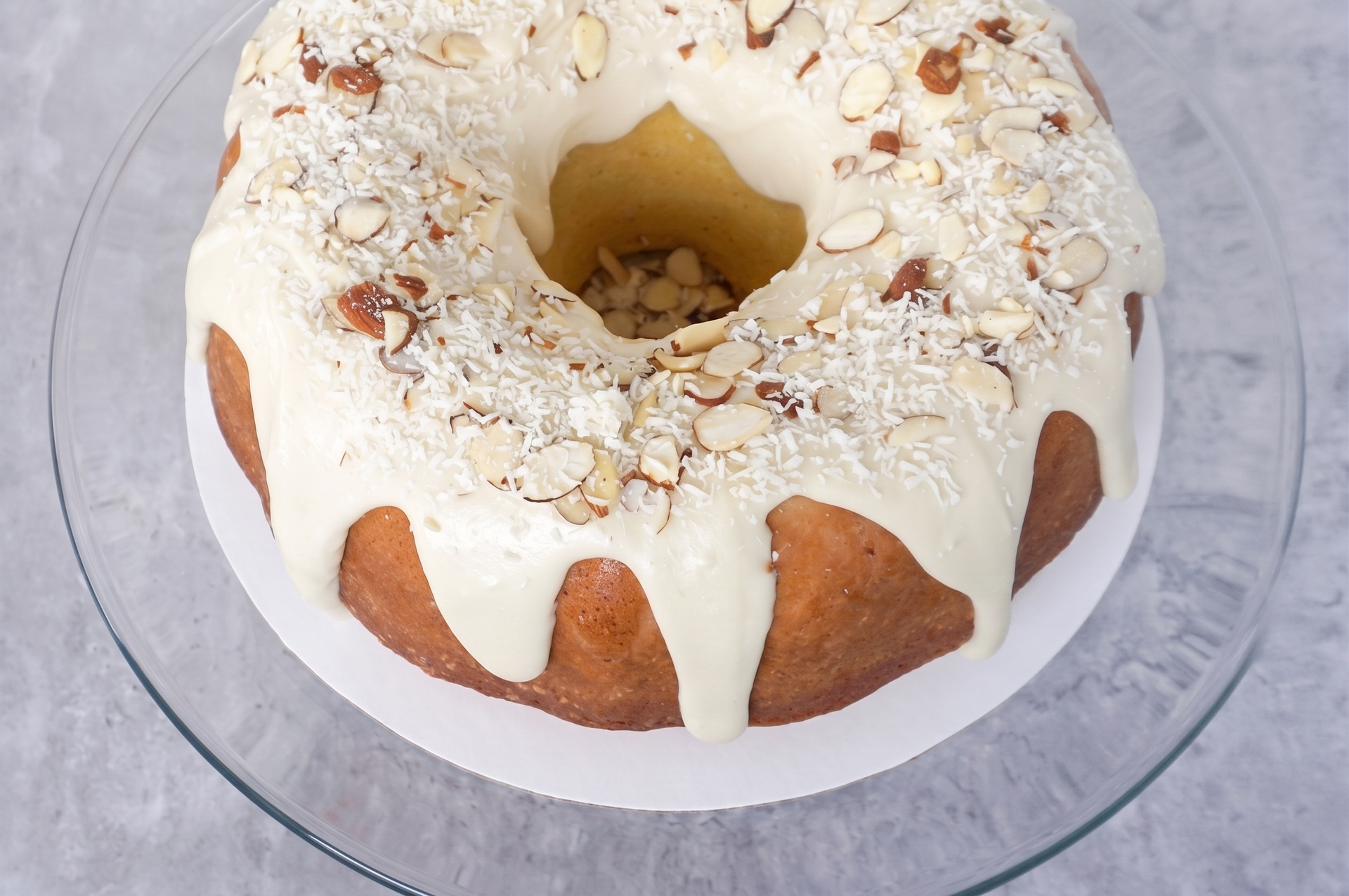 Powdered bundt cake with white glaze and sliced almonds on a glass stand