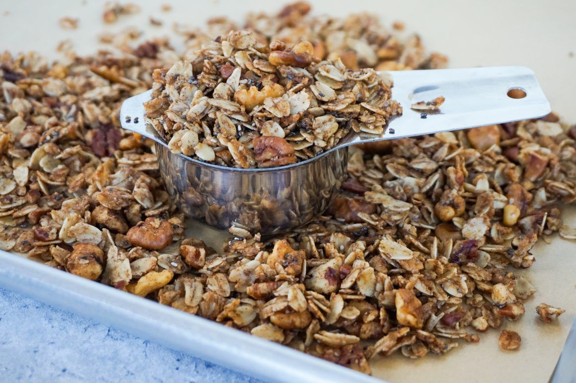Metal scoop in a tray of granola and oats on a counter
