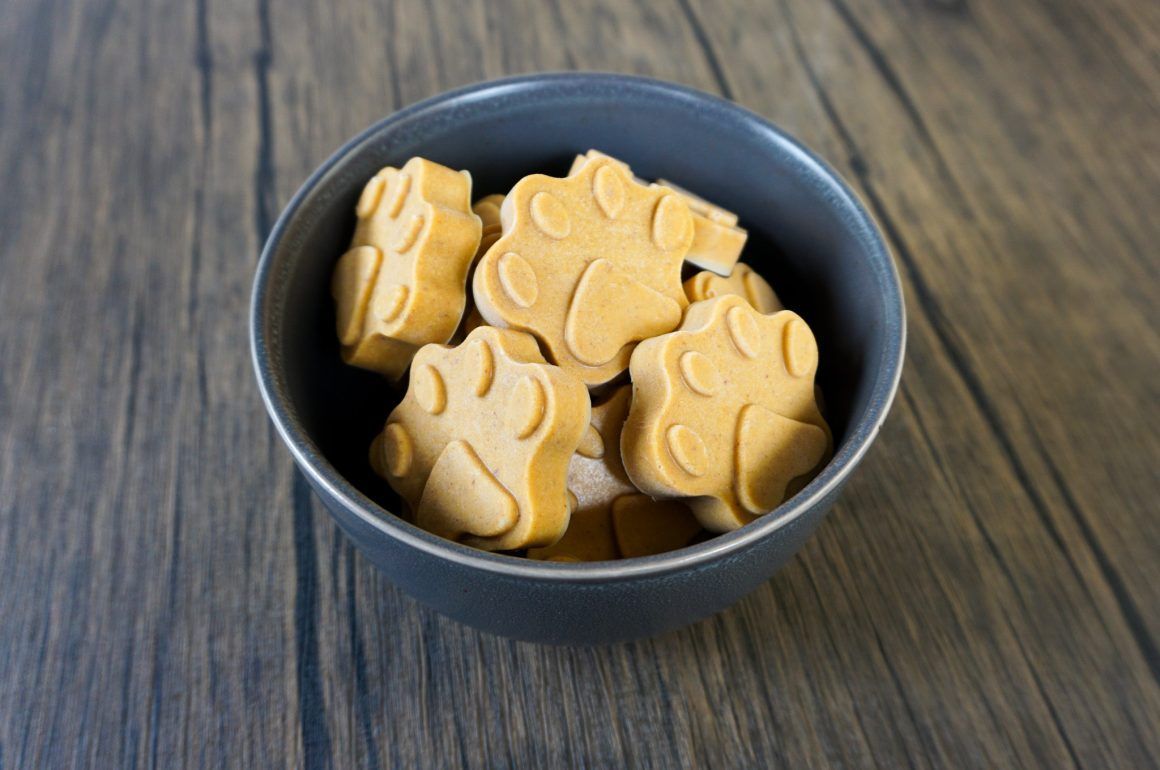 A black bowl filled with tan paw-shaped biscuits on a wooden table