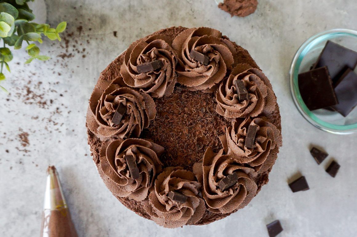Chocolate cake with rosette frosting, viewed from above on a light surface with chocolate pieces nearby