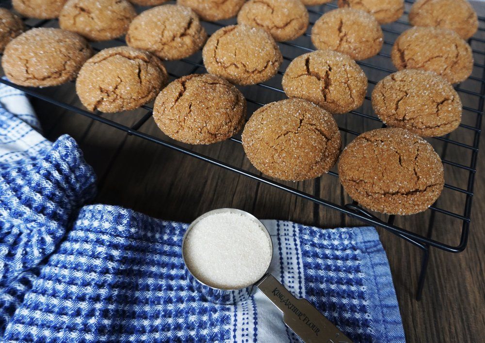 Freshly baked muffins cooling on a wire rack beside a spoonful of sugar and a blue checkered towel